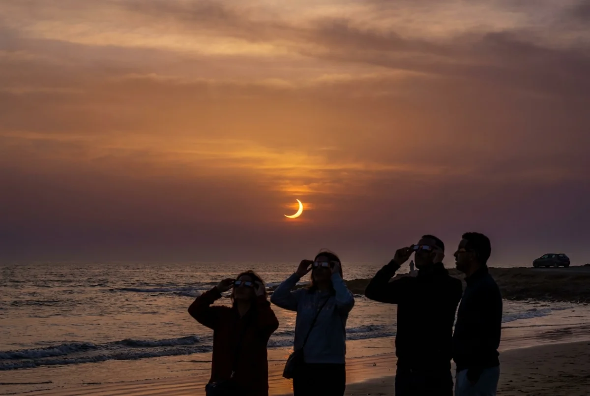 Éclipse solaire partielle du 12 août 2026 au coucher du soleil sur l'Atlantique près d'Agadir, observateurs avec lunettes de protection